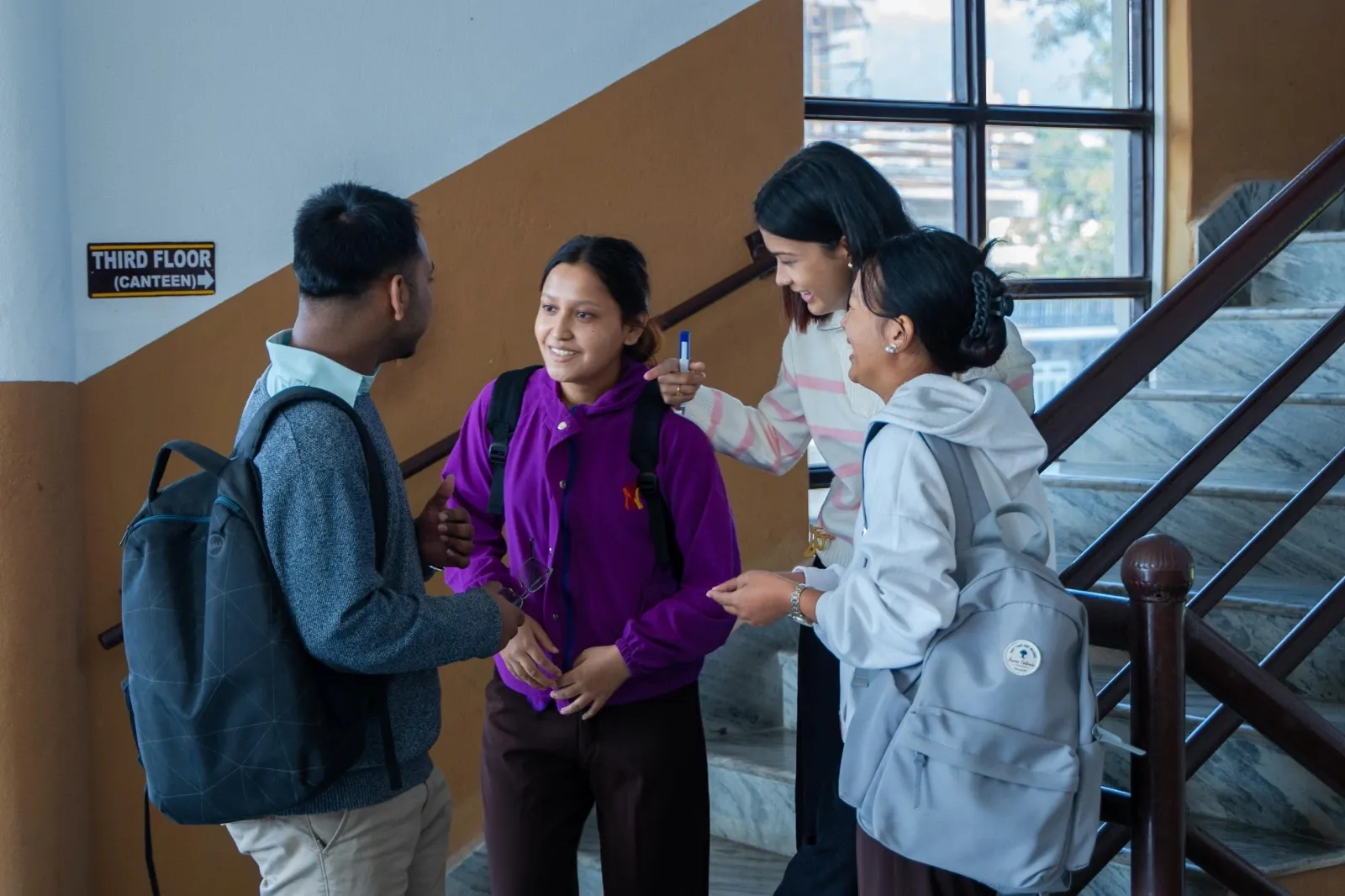 One boy and three girls standing talking by the staircase