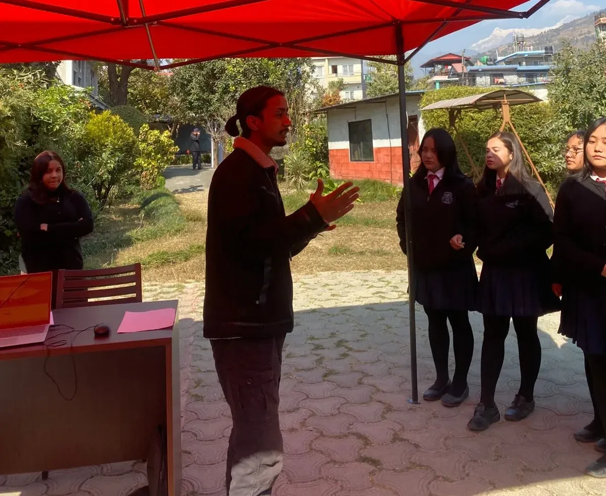 A boy standing infront of bunch of students explaining things.