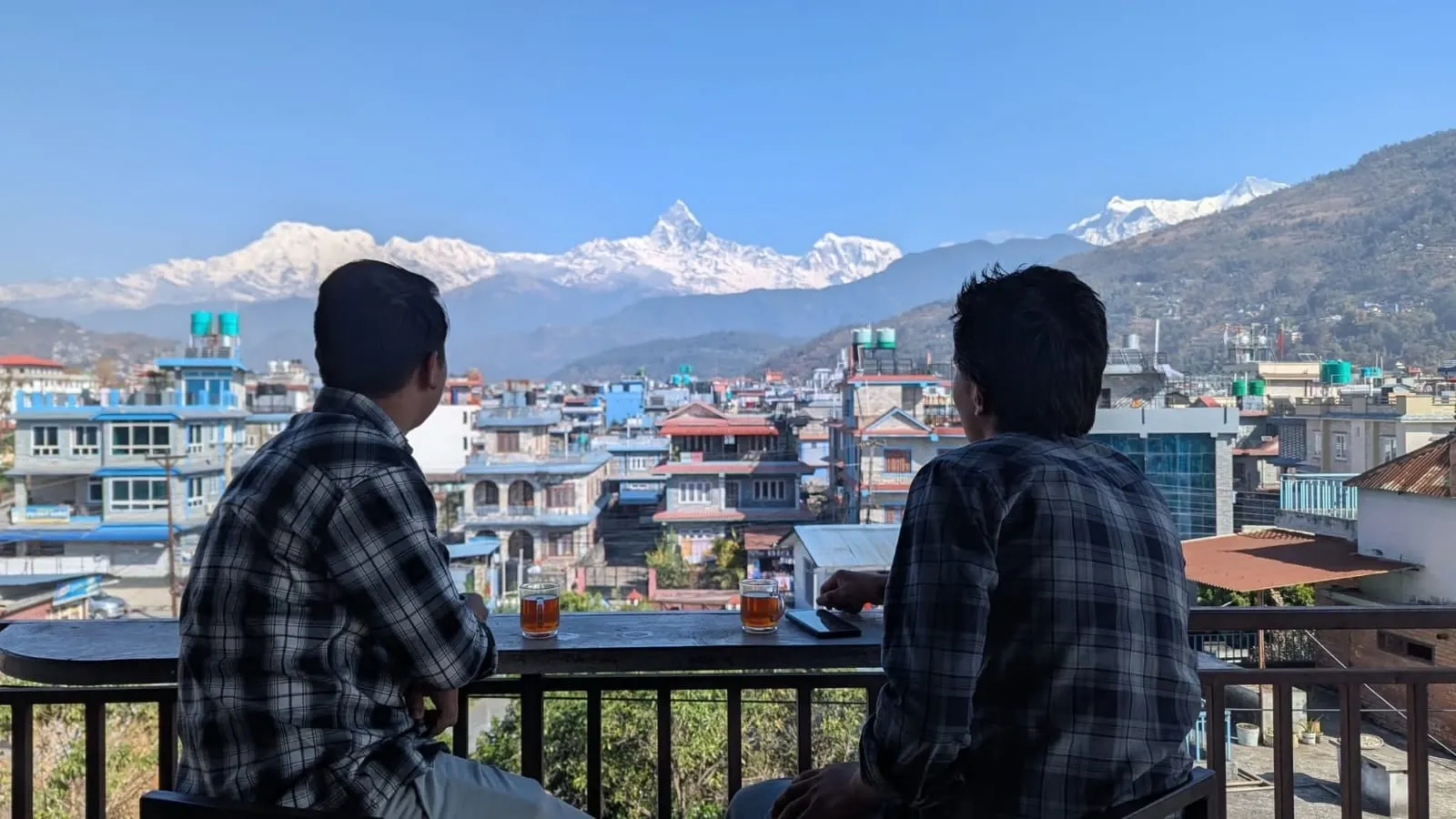 Two boy looking at a mountain view with cup of tea in a rooftop